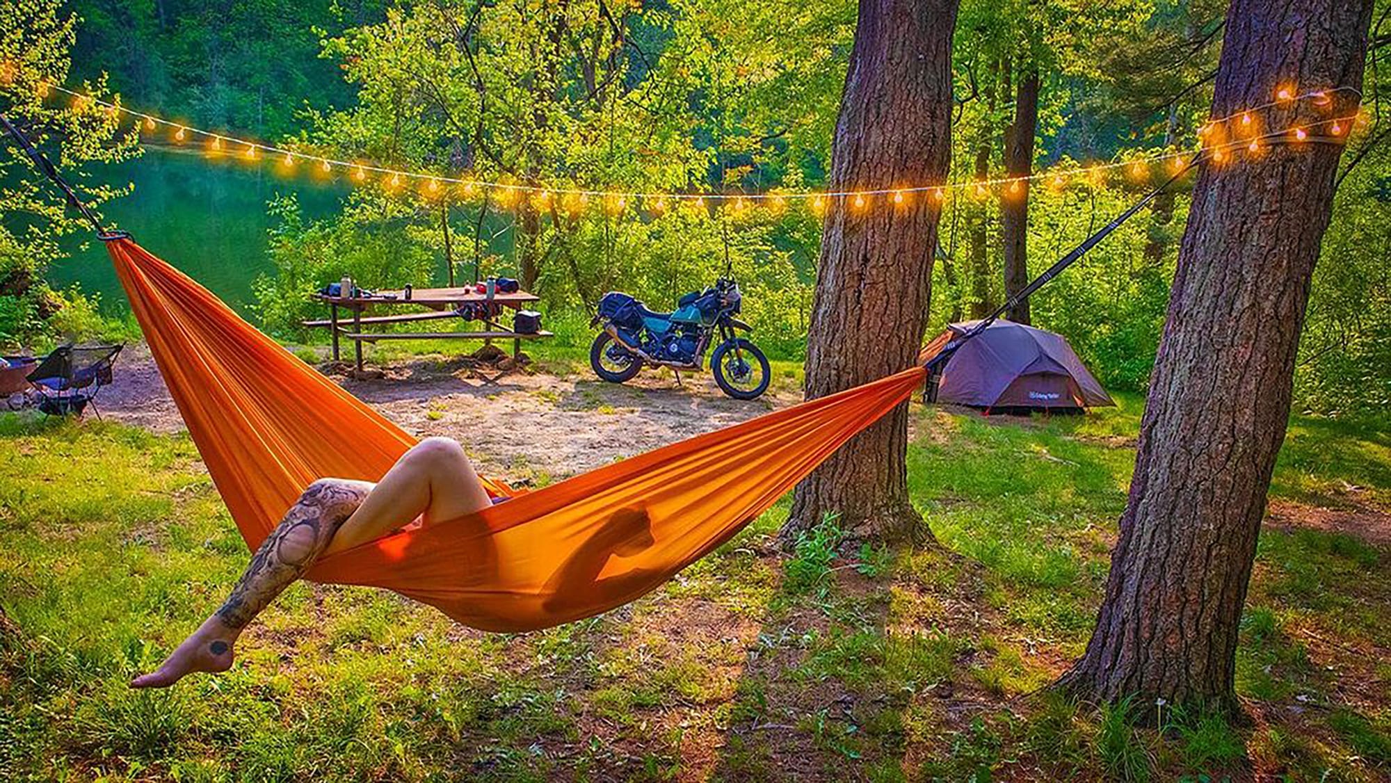 a woman in a hammock near a motorcycle and a tent