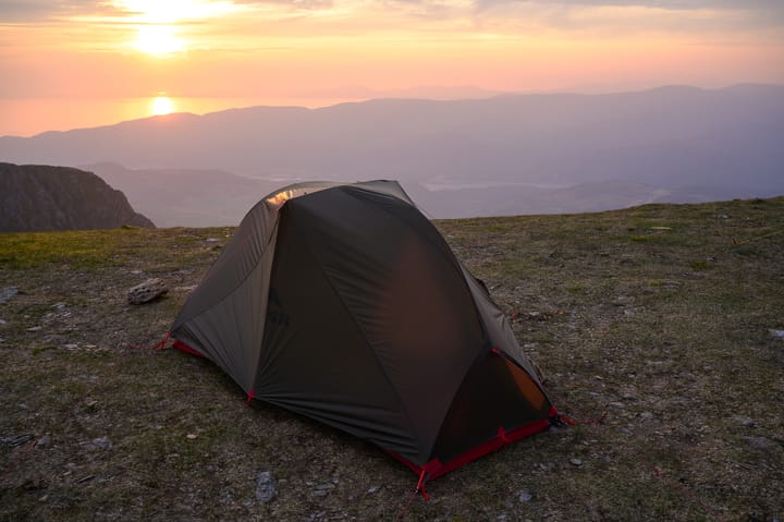 tent pitched on barren escarpment at sunset